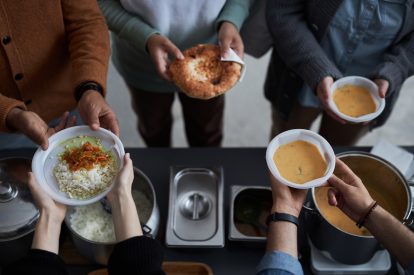 Top view closeup of unrecognizable volunteers giving out hot meals to people in need at soup kitchen, copy space
